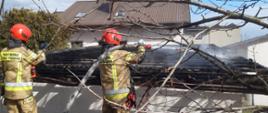 Zdjęcie przedstawia strażaków przelewających wodą spalony dach oraz mierzących temperaturę belek kamerą termowizyjną