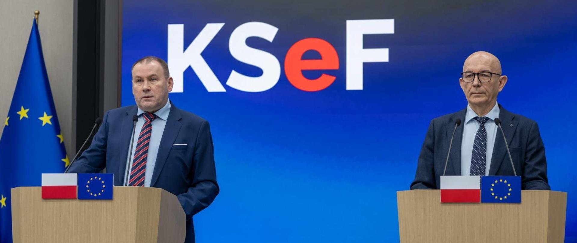 Zbigniew Stawicki, Podsekretarz Stanu w Ministerstwie Finansów, Zastępca Szefa Krajowej Administracji Skarbowej oraz Roman Łożyński, dyrektor Centrum Informatyki Resortu Finansów przy mównicach z flagami Polski i Unii Europejskiej na tle ekranu z logo KSeF