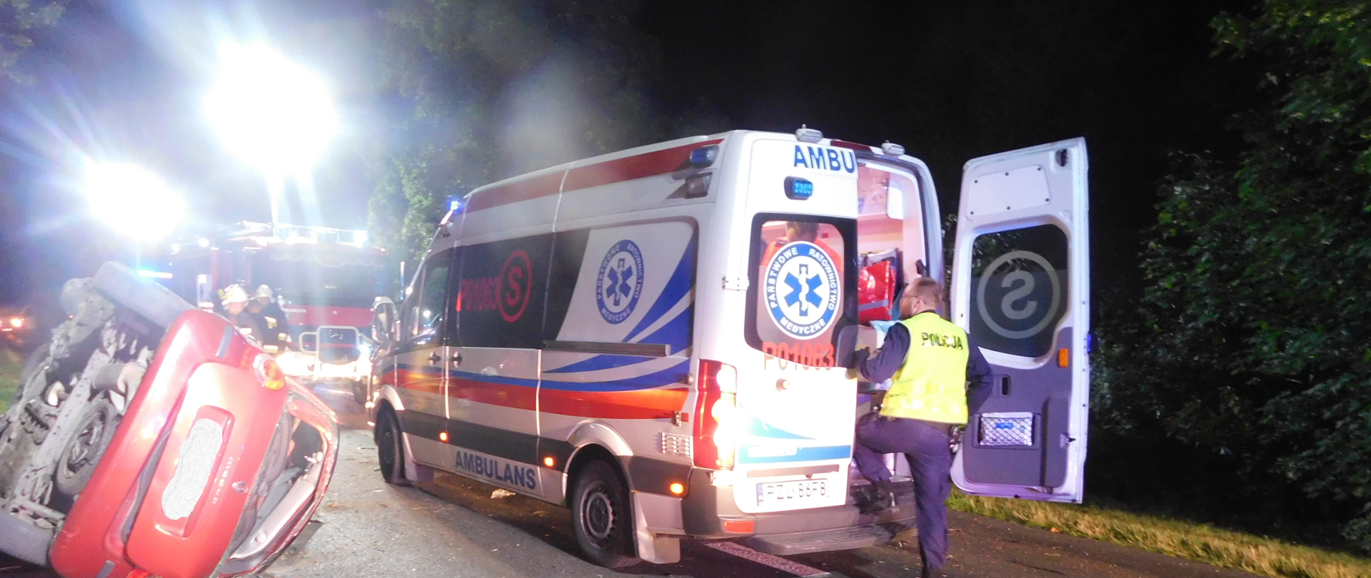 na zdjęciu samochód osobowy leżący na boku oraz karetka pogotowia stojąca na kołach