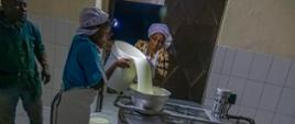 dwie kobiety przelewają mleko do zbiornika