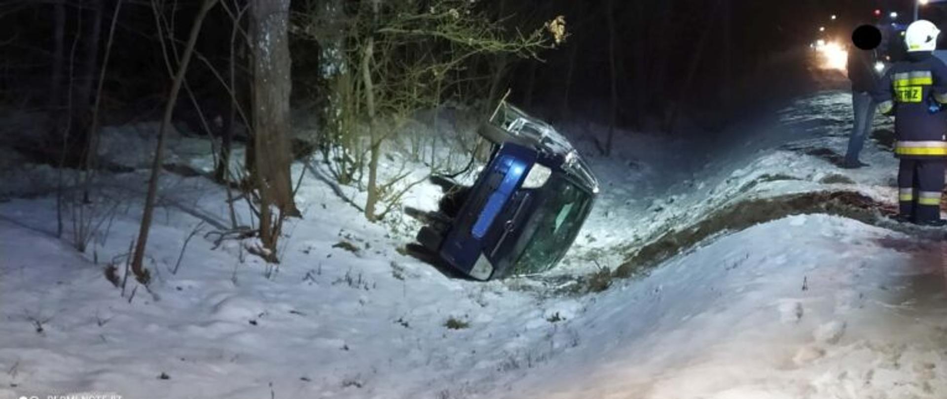 Widać samochód osobowy w rowie na lewym boku oraz jednego strażaka
