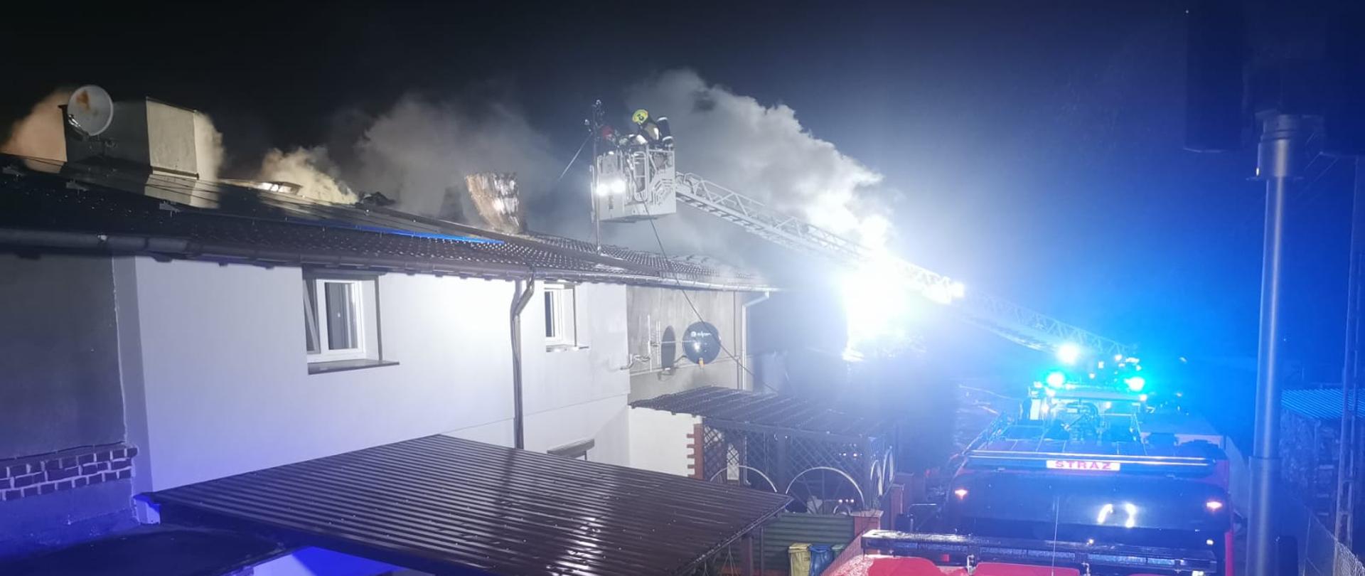 Na zdjęciu widać kompleks palących się budynków oraz strażaków działających w koszu drabiny mechanicznej 