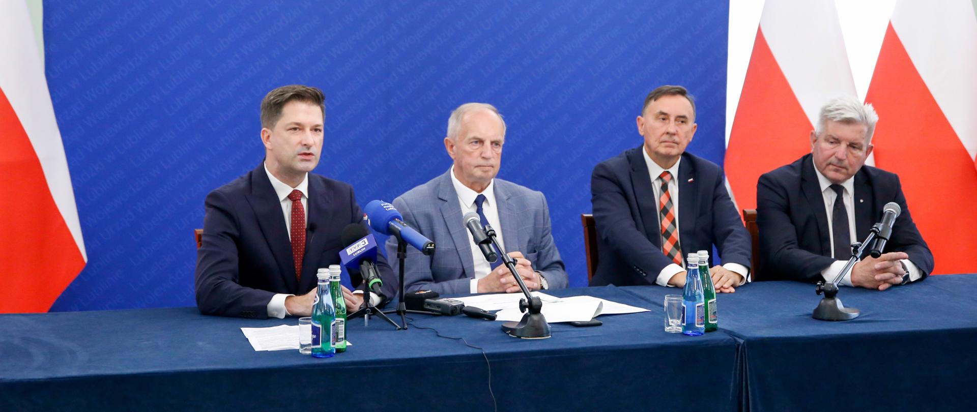 Wicewojewoda lubelski wraz z trzema posłami siedzą za stołem prezydialnym podczas briefingu prasowego.