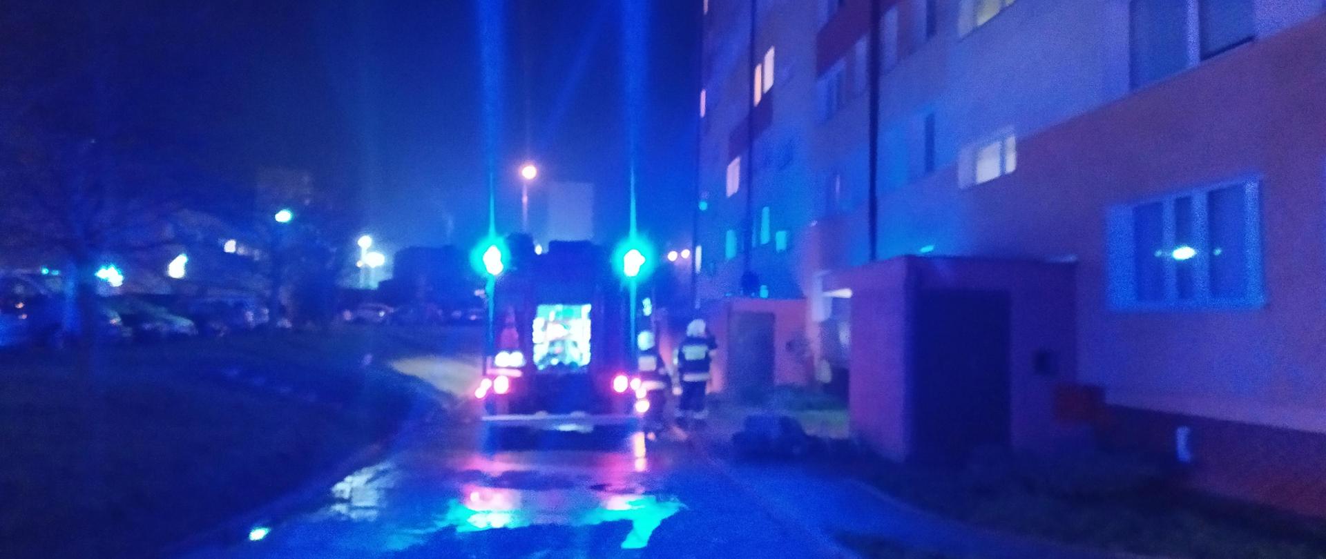zdjęcie przedstawia pojazd strażacki na miejscu pożaru, w tle jest blok