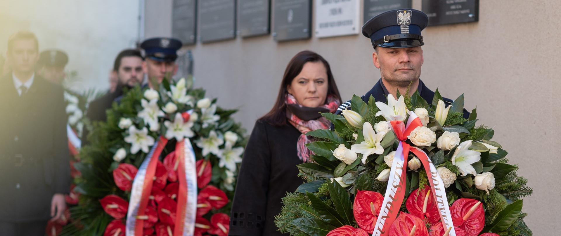 Żołnierze trzymają w rekach wieńce. Za nimi stoją osoby. Wśród nich wiceminister Małgorzata Jarosińska-Jedynak.