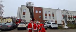 Parking przy szpitalu. Na środku zdjęcia Mikołaj z workiem i dwiema kobietami przebranymi za Mikołaje, za Nimi samochód z drabiną mechaniczną.