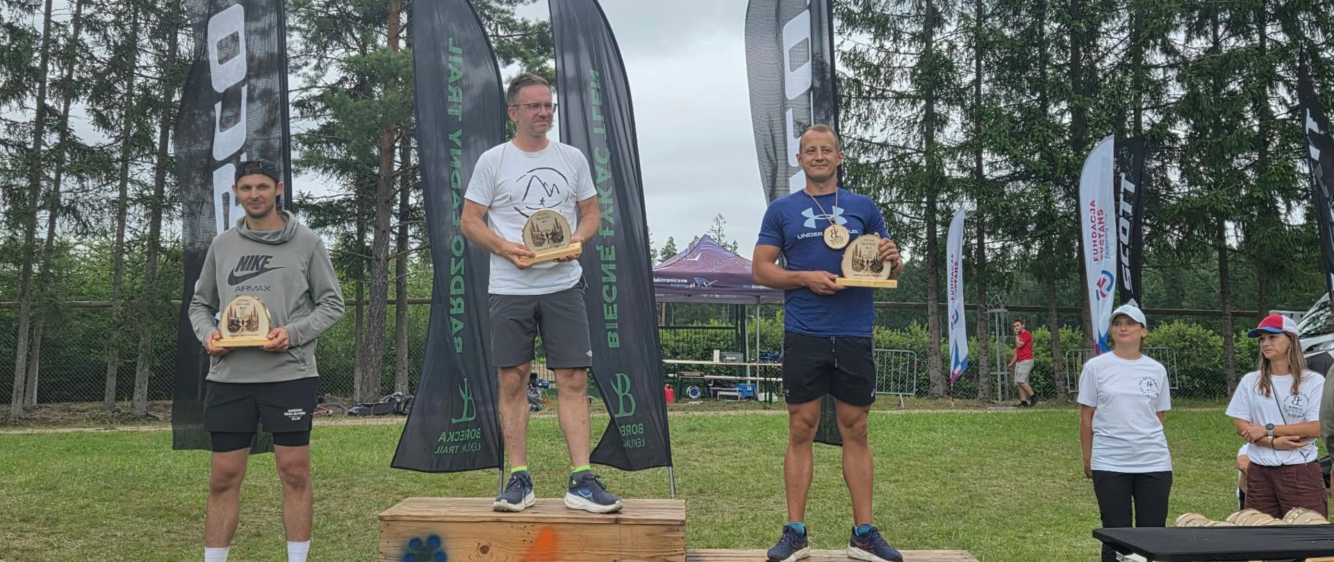 Laureaci biegów stojący na podium zawodów. Strażak reprezentujący KP PSP w Olecku stoi na 2 miejscu podium.