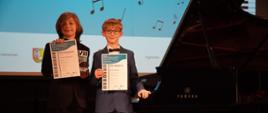 Chłopcy na scenie przy fortepianie trzymają dyplomy Międzynarodowy Konkurs Pianistyczny w Libiążu