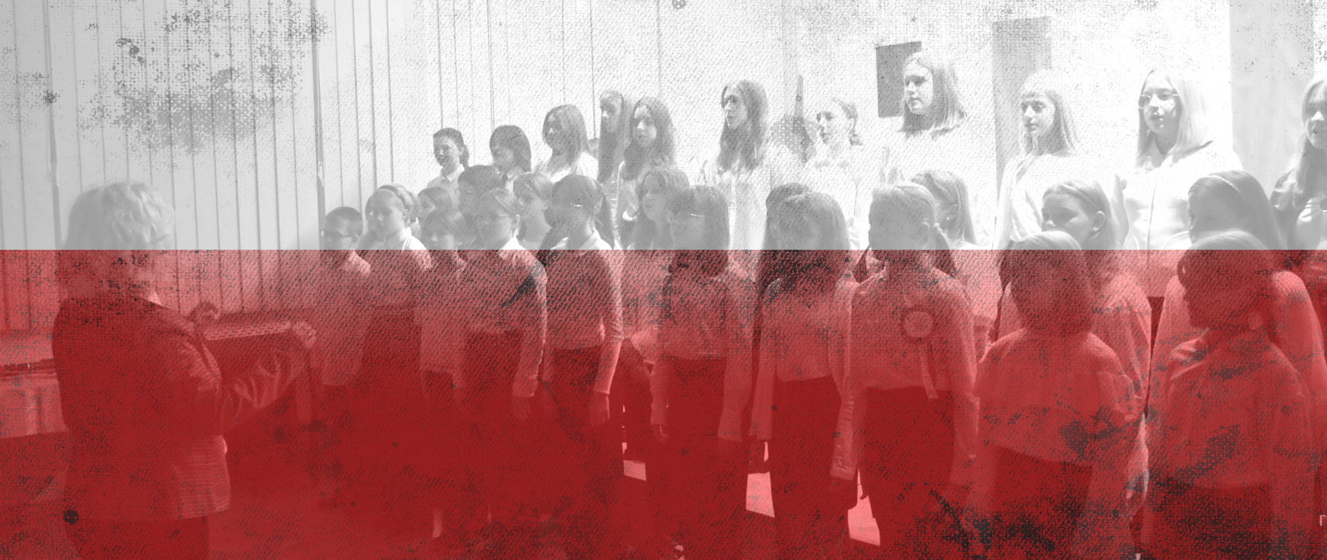 Chór szkolny prowadzony przez p. Beatę Drabik-Sowa na tle flagi biało-czerwonej.