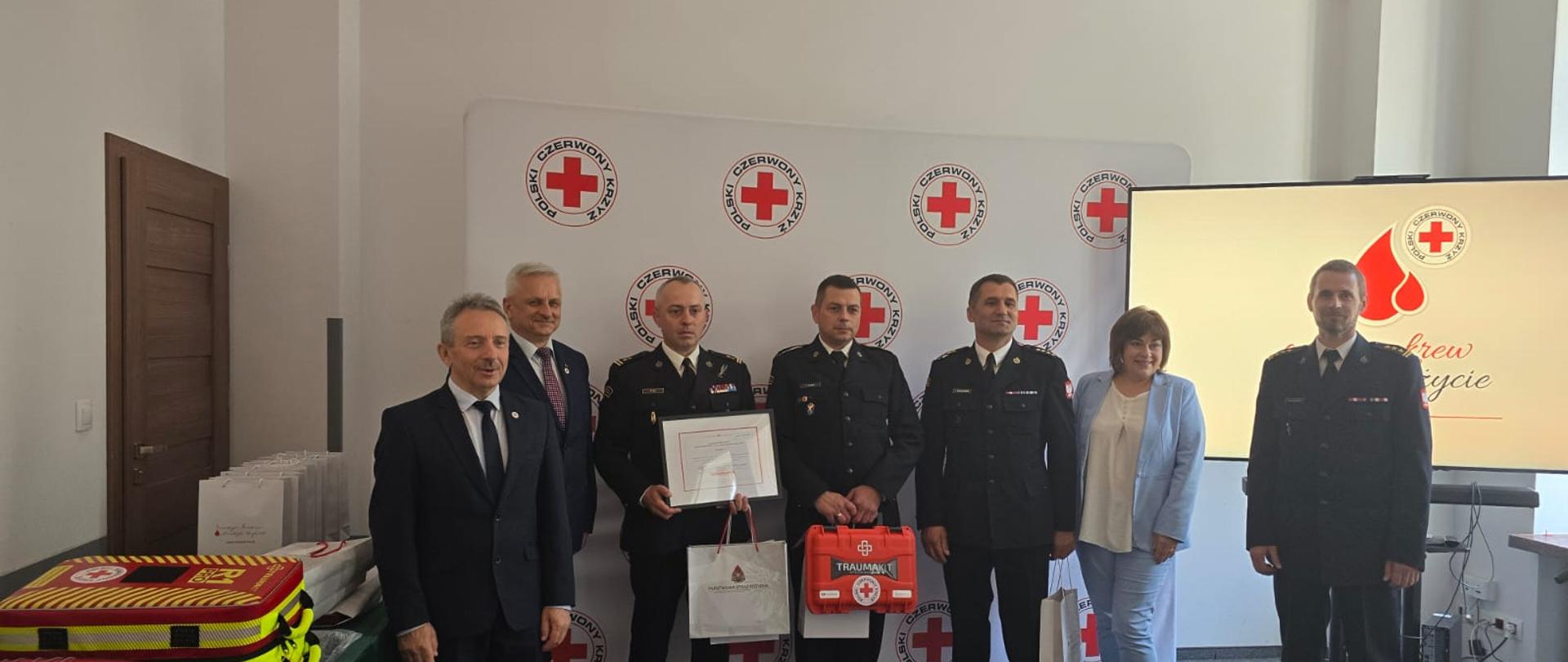 Zdjęcie przedstawia wręczenie nagród KP PSP w Kartuzach podczas finału akcji ognisty ratownik - gorąca krew. Na zdjęciu obecni są przedstawiciele polskiego czerwonego krzyża oraz komendy głównej psp.