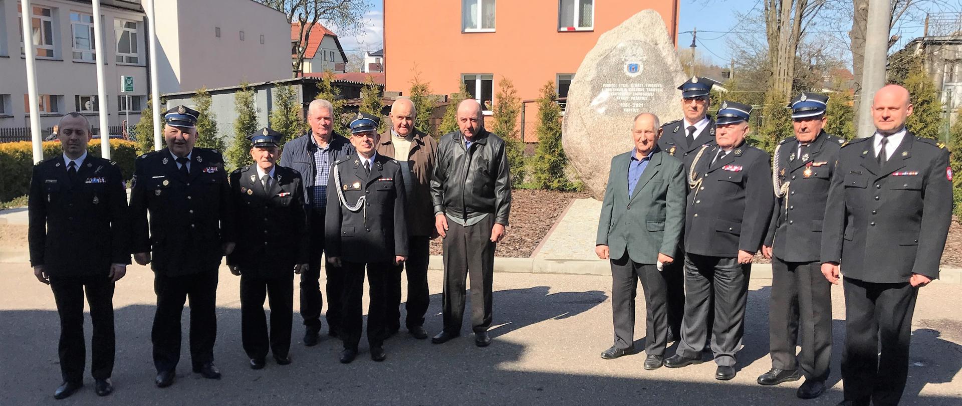 Zdjęcie grupowe uczestników uroczystości na tle obelisku na placu KP PSP w Kartuzach.