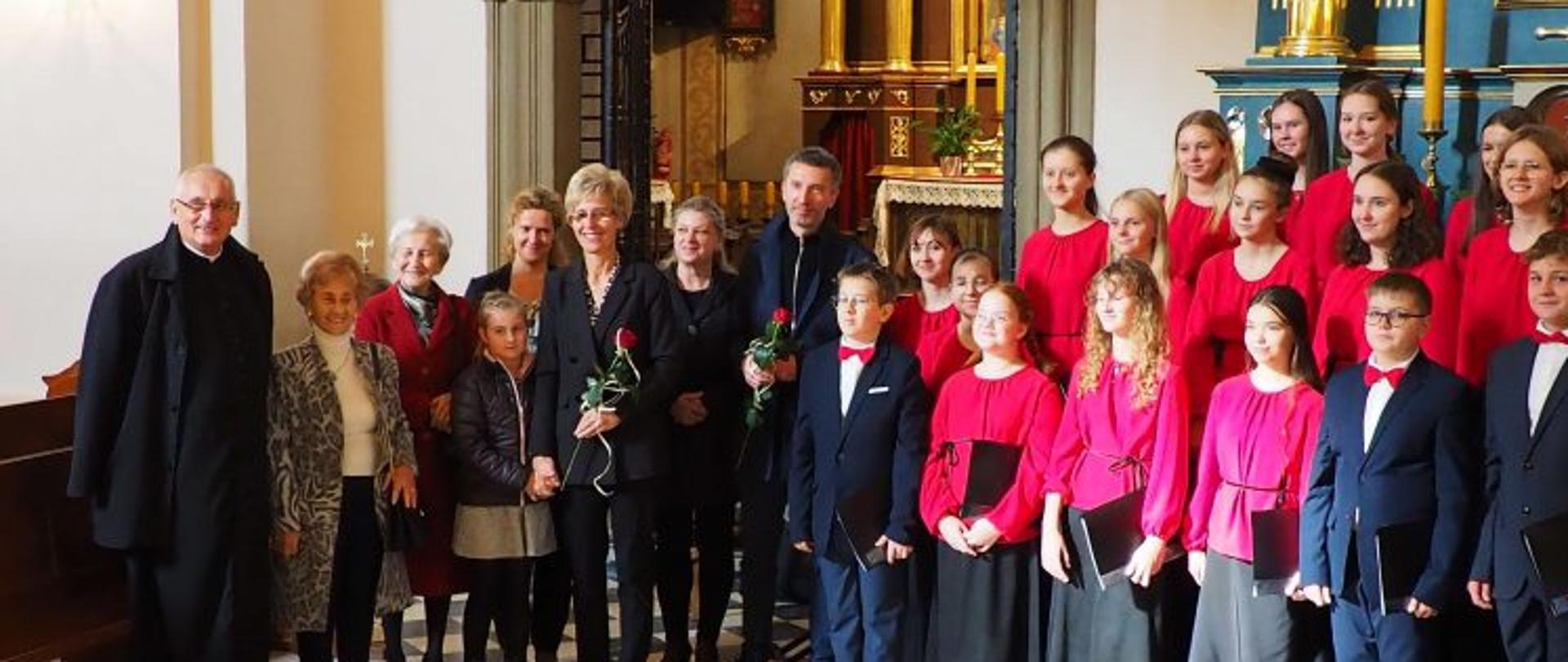 Od lewej stoją: ks. Proboszcz Parafia Narodzenia NMP w Myślenicach, dwie Panie z KiK, Pani V-ce Dyrektor PSM mgr Agnieszki Tyrały, Pani dyrygent mgr Moniki Szymskiej, Pani Dyrektor PSM mgr Jolanta Antkiewicz, Pan mgr Piotra Skupniewicza - kierownik zespołu klarnetowego, Dzieci zespołu Cantata i zespołu klarnetowego.