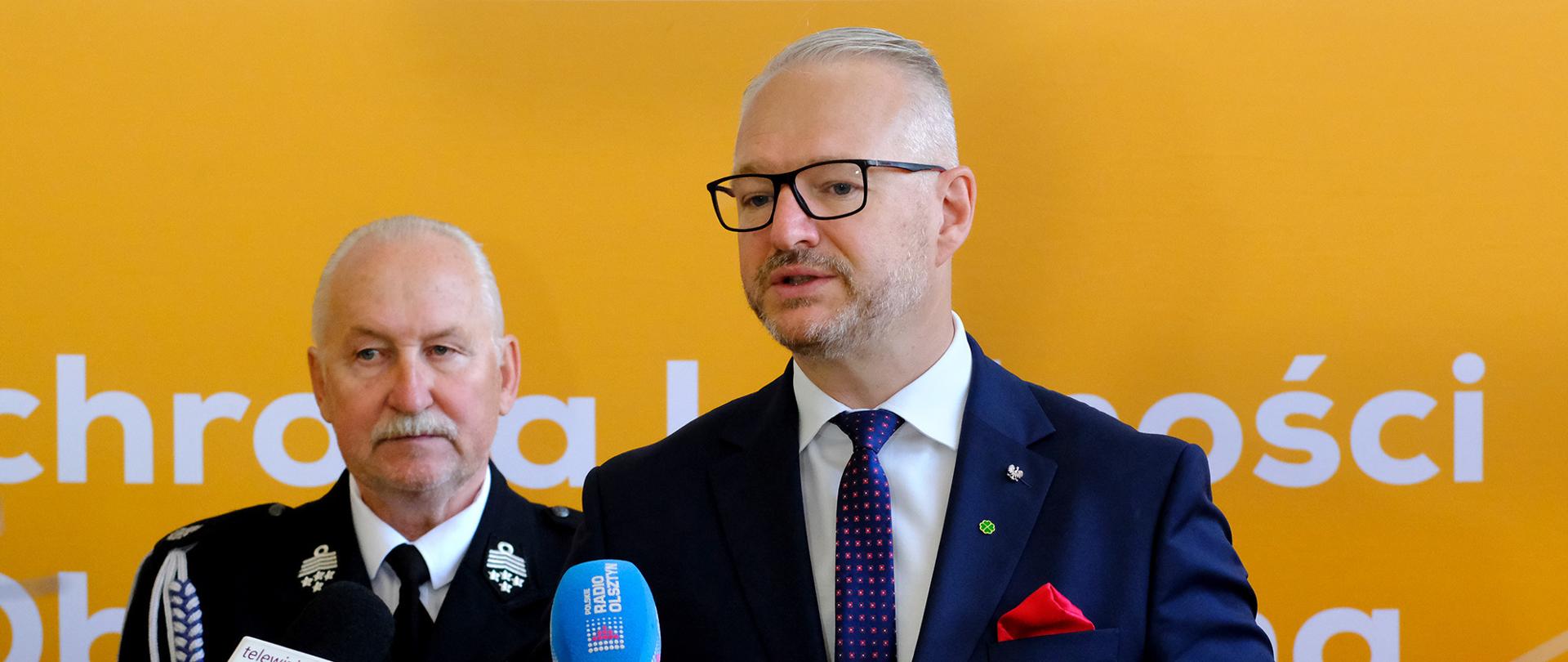 Mężczyzna w garniturze na tle żółtej ścianki trzyma w rękach książeczkę 