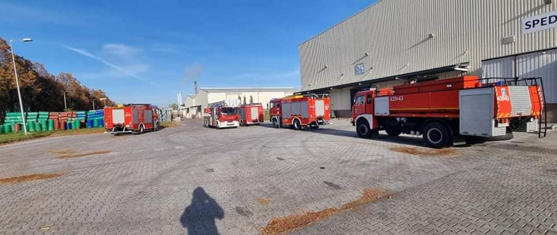 Zdjęcie przedstawia samochody pożarnicze stojące na placu zakładu produkcyjnego.