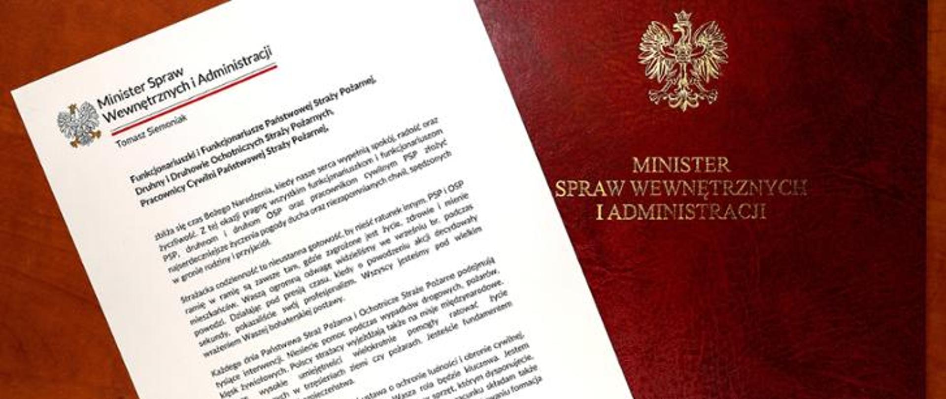 Na grafice przedstawiono list gratulacyjny podpisany przez Ministra Spraw Wewnętrznych i Administracji oraz okolicznościową teczkę z godłem Rzeczypospolitej Polskiej i napisem „Minister Spraw Wewnętrznych i Administracji”. Dokument oraz teczka ułożone są na drewnianym blacie. Grafika nawiązuje do wyróżnienia lub podziękowania skierowanego do funkcjonariusza Państwowej Straży Pożarnej.