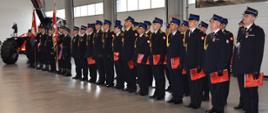 Na zdjęciu znajduje się grupa osób stojących w hali jednostki straży pożarnej. Uczestnicy trzymają wyróżnienia. W tle widoczni są strażacy w mundurach galowych oraz baner Komendy Powiatowej PSP w Jarosławiu.