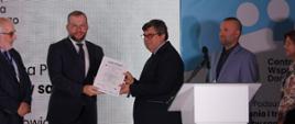 Minister funduszy i polityki regionalnej Grzegorz Puda wręcza certyfikat uczestnictwa w projekcie Centrum Wsparcia Doradczego Plus, minister trzyma w rękach certyfikat i wręcza go jednemu z uczestników projektu