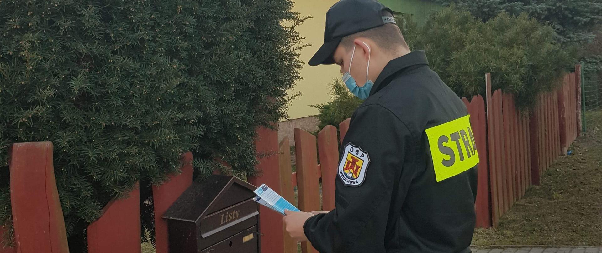 Zdjęcie przedstawia strażaka wkładającego ulotki do skrzynki na listy