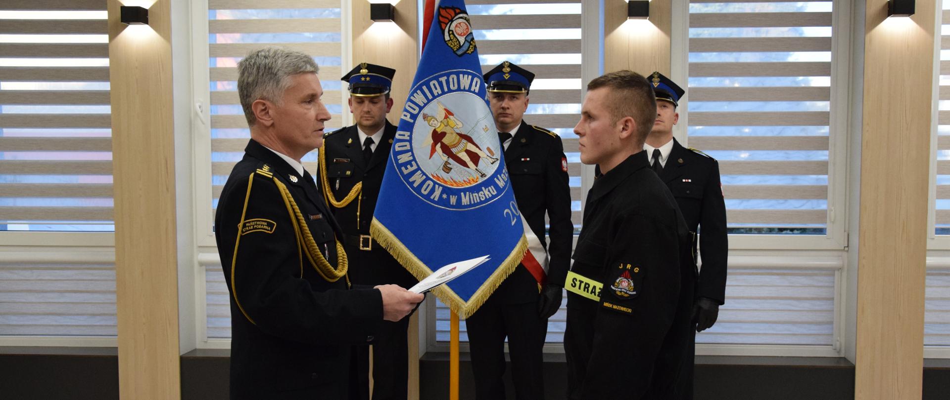 Nowy funkcjonariusz str. Rafał Olko po ślubowaniu, Komendant Powiatowy PSP w Mińsku Mazowieckim przekazuje na jego ręce akt ślubowania i gratulacje oraz życzenia spokojnej służby w szeregach PSP.
