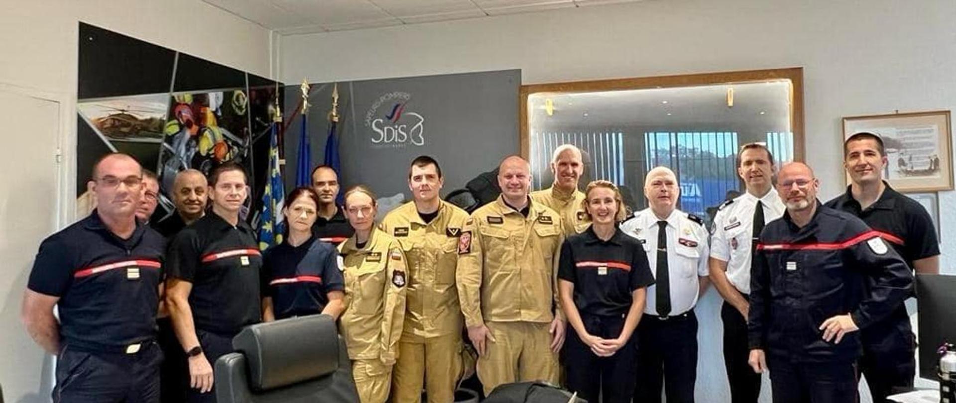 Grupa strażaków polskich i francuskich w mundurach stoi w biurze , na drzwiach napis SDiS