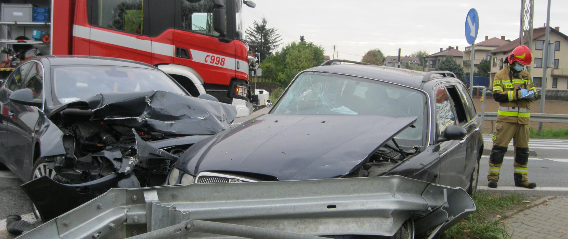 na miejscu widoczny jest jeden samochód PSP, oraz dwa uszkodzone pojazdy osobowe. Obok strażak spisujący informacje. 