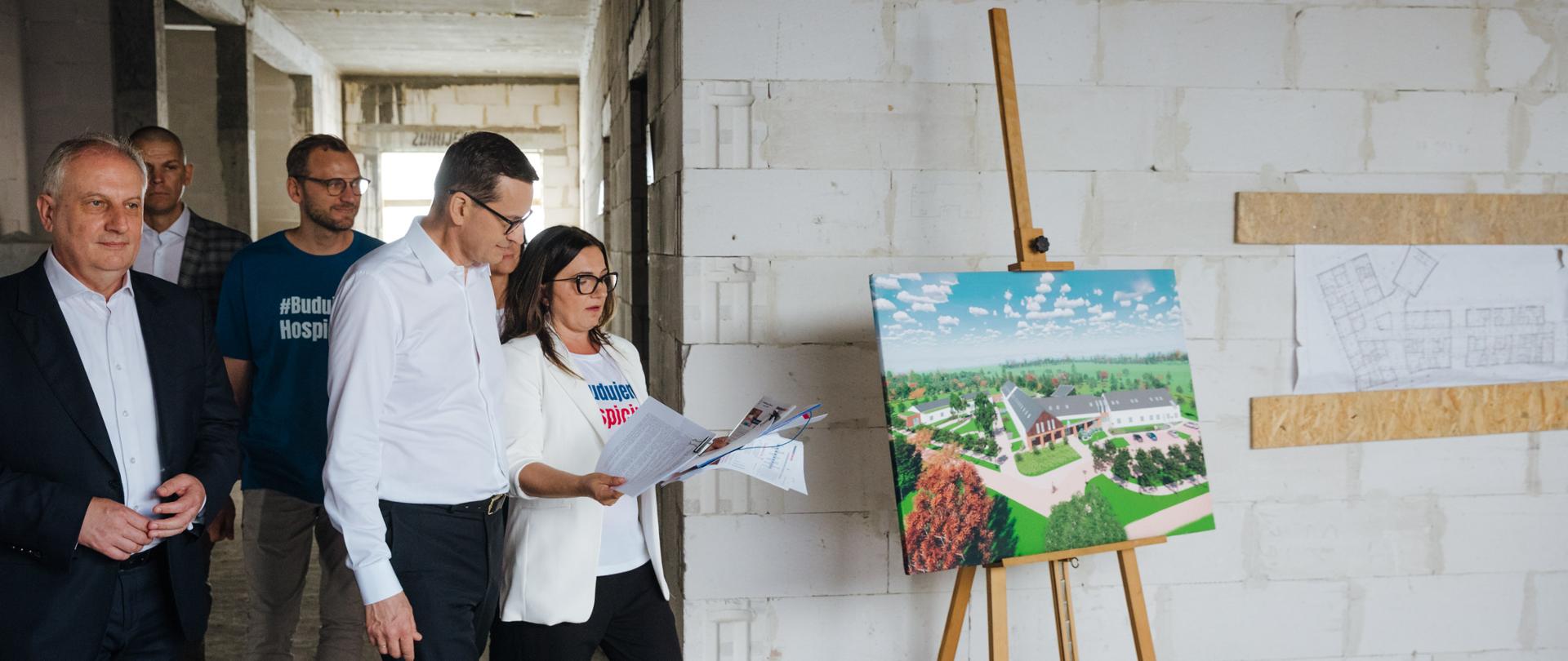 Prezes hospicjum oraz premier idą po budowie hospicjum.
