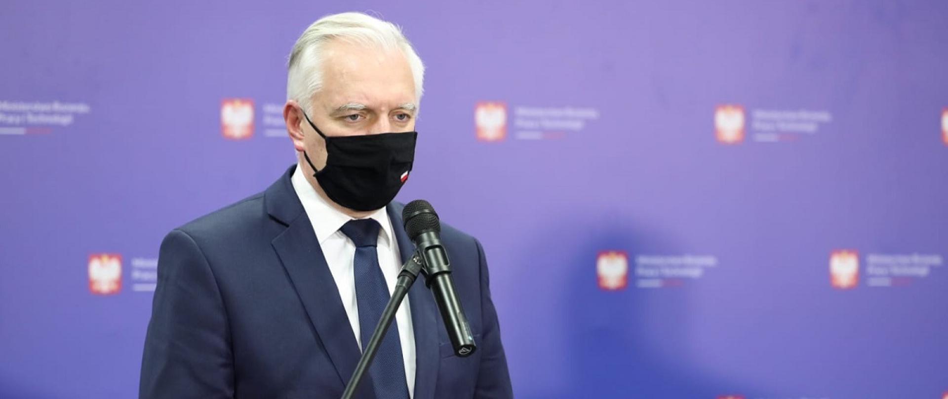 Wicepremier, minister rozwoju, pracy i technologii Jarosław Gowin stojący w maseczce na twarzy przy pulpicie