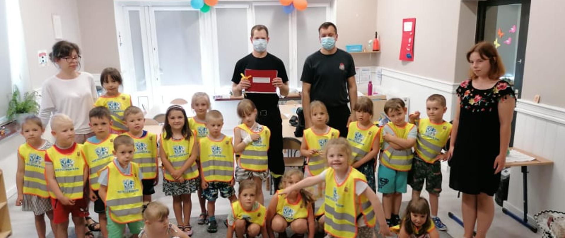Na zdjęciu znajdują się dzieci z Akademii Wiedzy i Zabawy wraz z opiekunami i strażakami.