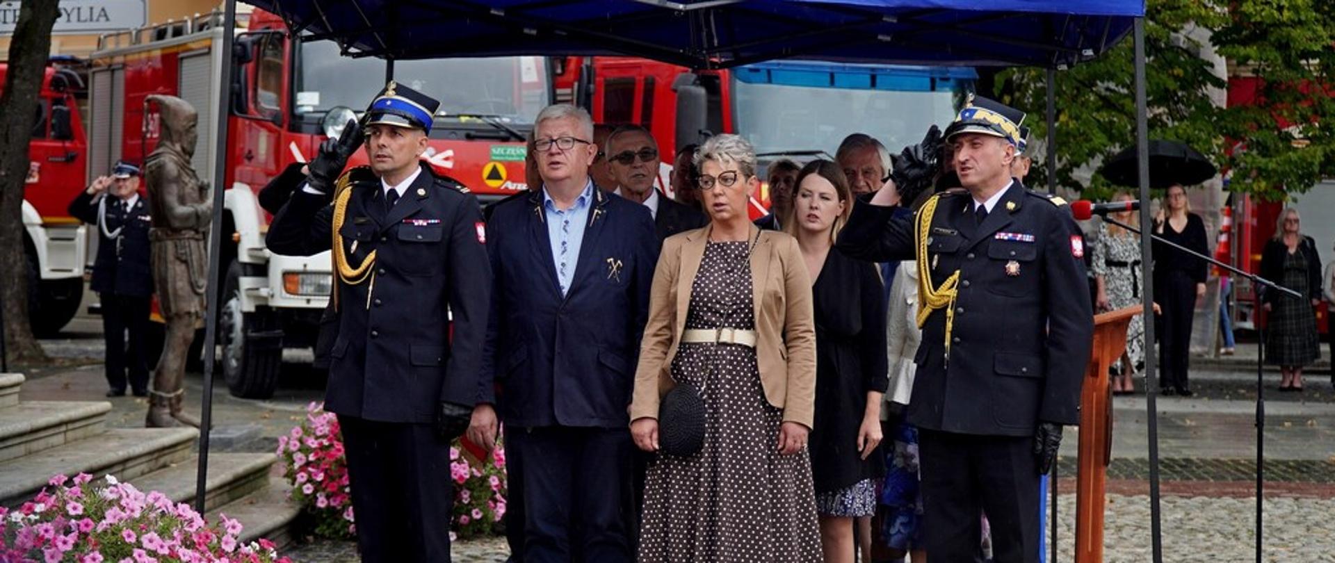 Na zdjęciu widoczni zaproszeni goście na uroczystym apelu połączonym z poświęceniem i przekazaniem czterech samochodów pożarniczych i quada dla jednostek Ochotniczych Straży Pożarnych z gminy Biecz. Pod niebieskim namiotem stają ministrowie, posłowie, samorządowcy strażacy PSP w tym Małopolski Komendant Wojewódzki i Komendant Powiatowy PSP w Gorlicach i OSP w tym Członek Zarządu Głównego Związku OSP RP i Prezes Zarządu Oddziału Powiatowego Związku OSP RP w Gorlicach