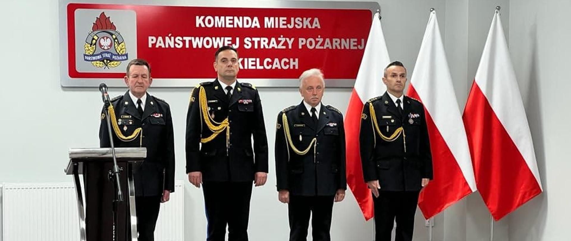 Na zdjęciu widzimy czterech mężczyzn stojących w szeregu w mundurach strażackich.
