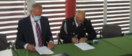 Za zdjęciu moment podpisania umowy. Przy stole prezydialnym po lewej stronie siedzi Pan Andrzej Skiba Prezes Zarządu Wojewódzkiego Funduszu Ochrony Środowiska i Gospodarki Wodne w Rzeszowie trzymając w prawej ręce długopis i umowę. Po prawej stronie Prezes Ochotniczej Straży Pożarnej w Gliniku Średnim siedząc przy stole podpisuje umowę. Obaj Panowie w maseczkach ochronnych. Na stole w kolorze zielonym widać od lewej strony: białą teczkę na dokumenty, mikrofon, czarą teczkę na dokumenty, dwie umowy oraz pieczątkę.