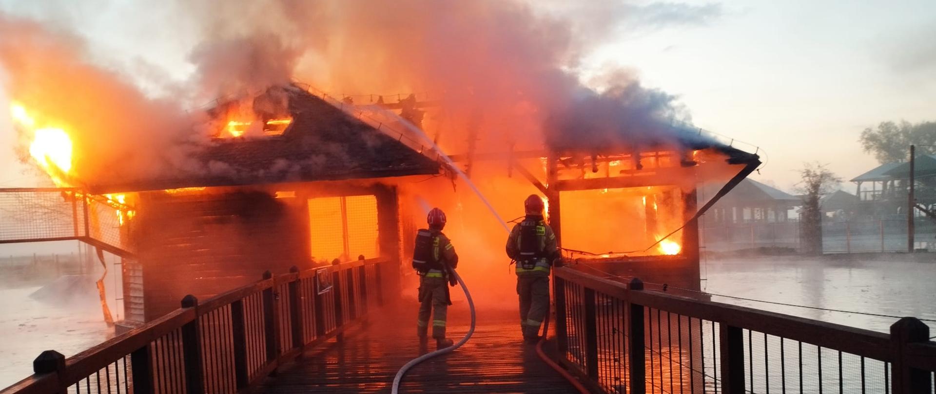 Dwóch strażaków gasi palący się budynek