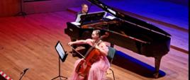 Dziewczyna gra na wiolonczeli, za nią mężczyzna gra na fortepianie.