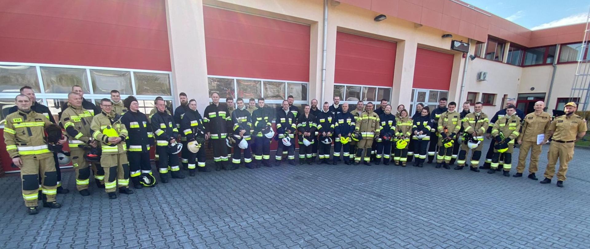 Zdjęcie przedstawia druhów OSP uczestniczących w egzaminie w KP PSP Międzyrzecz, wraz z funkcjonariuszami PSP – członkami komisji egzaminacyjnej na placu ćwiczeń.