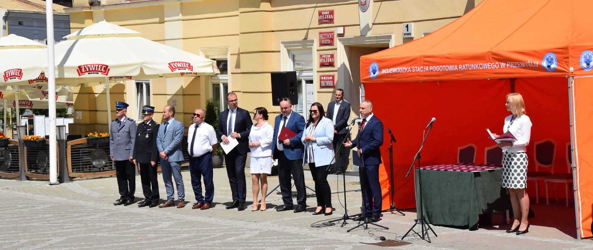 Rynek w Przemyślu, obok siebie w rzędzie stoi 9 osób.