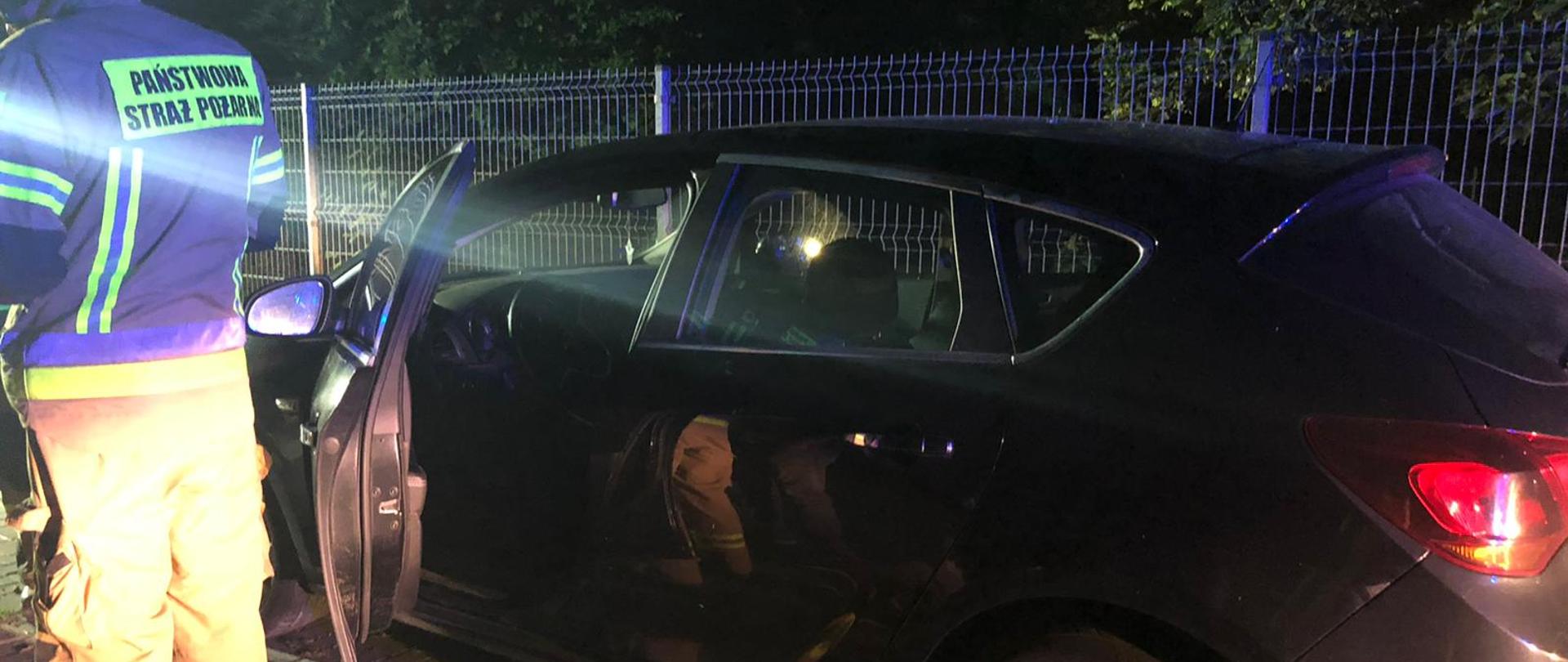 Na zdjęciu samochód. Zdjęcie w porze nocnej. Po lewej stronie ratownik w ubraniu specjalnym, piaskowym i hełmie.