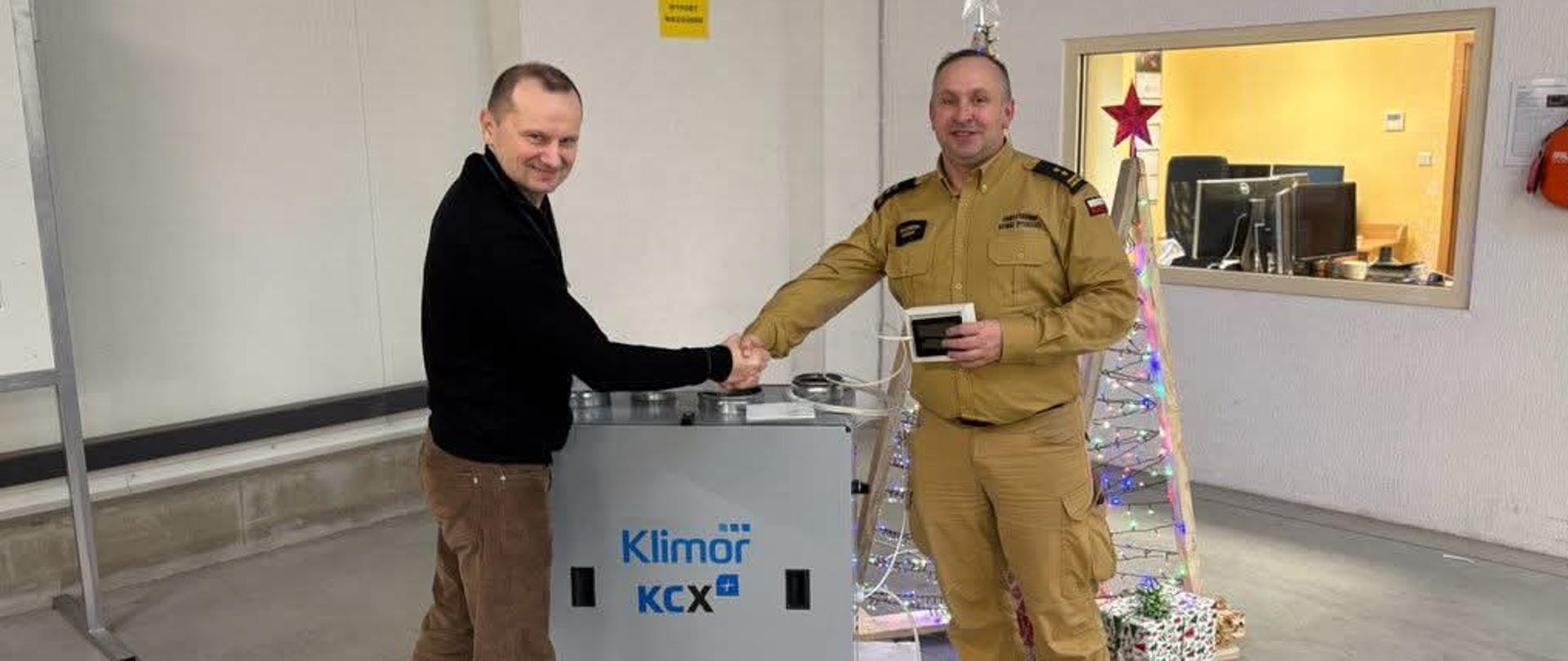 Na zdjęciu Komendant Powiatowy PSP w Pucku bryg. Wojciech Wanat oraz przedstawiciel firmy Klimor- centrale klimatyzacyjne i wentylacyjne. Komendant ubrany w strój służbowy w kolorze piaskowym. 