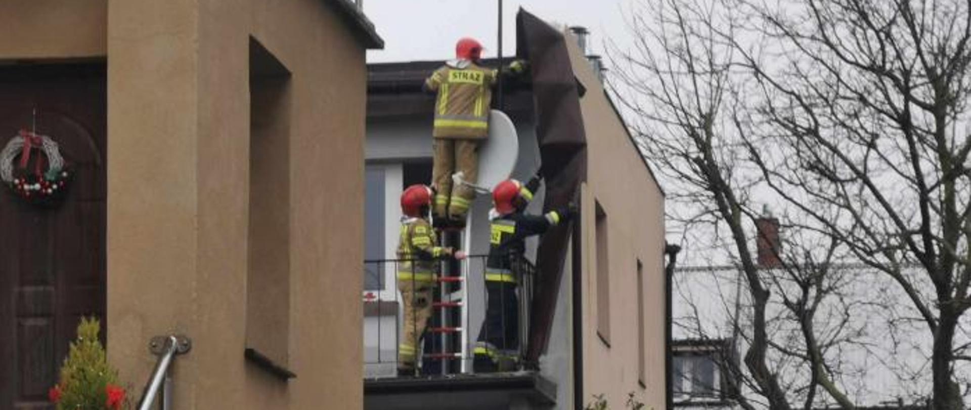 czterech strażaków na balkonie domu usuwa uszkodzone poszycie dachu