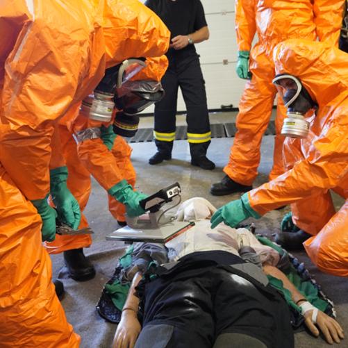 Uczestnicy szkolenia w kombinezonach i maskach ochronnych badają fantom