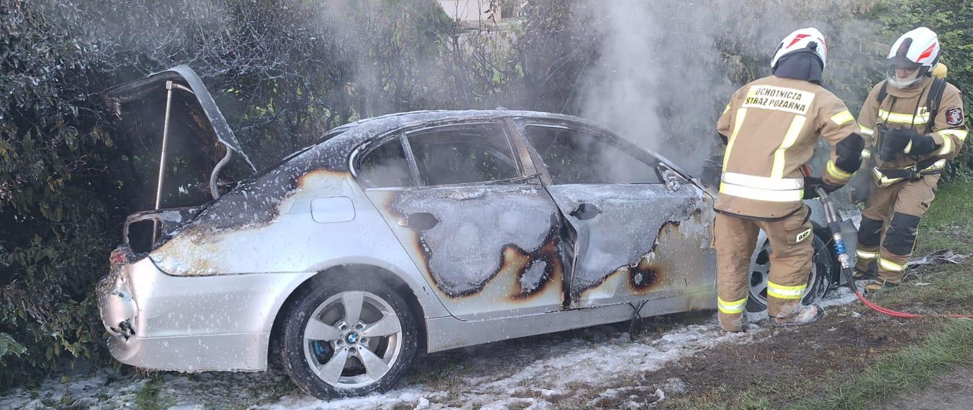 Strażacy prowadzą działania przy spalonym samochodzie.