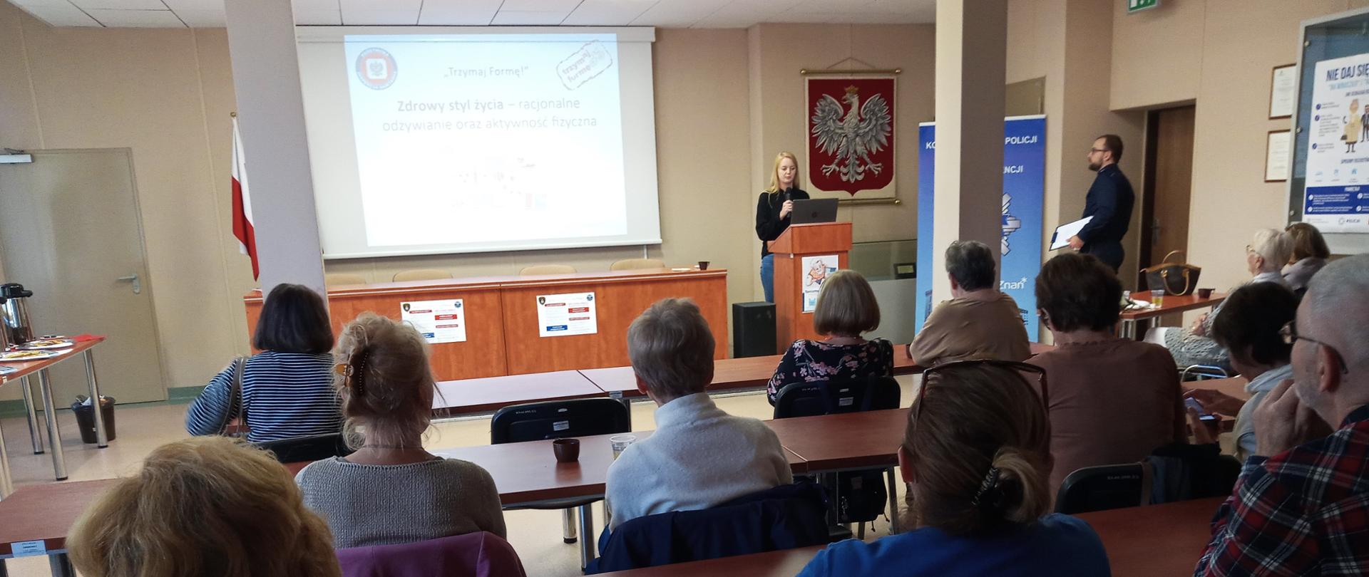 Pracownik PSSE na podstawie prezentacji multimedialnej wygłasza wykład o racjonalnym odżywianiu dla zebranych seniorów oraz pracowników Policji.