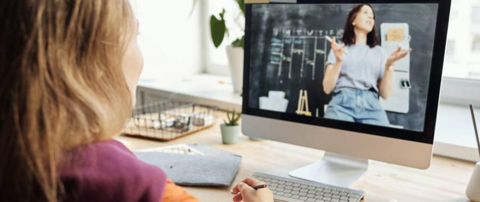 Kobieta patrzy na ekran komputera na którym widzi kobietę, która prowadzi szkolenie lub wykład
