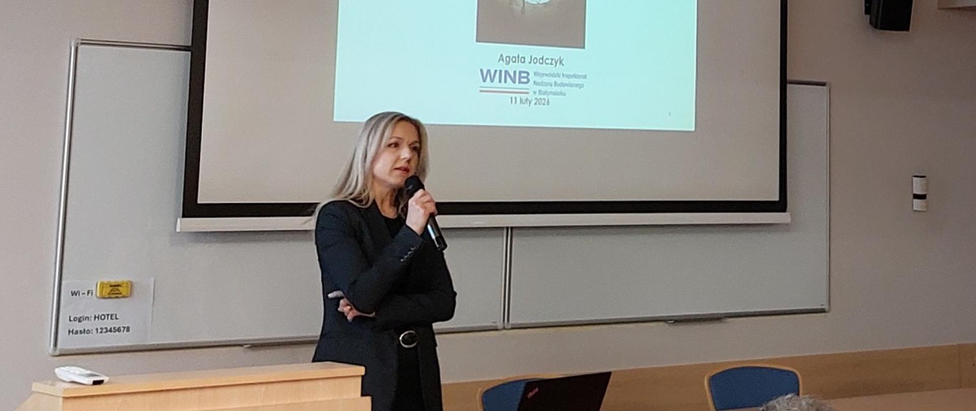 Kobieta prowadzi prezentację przed zgromadzoną publicznością. 