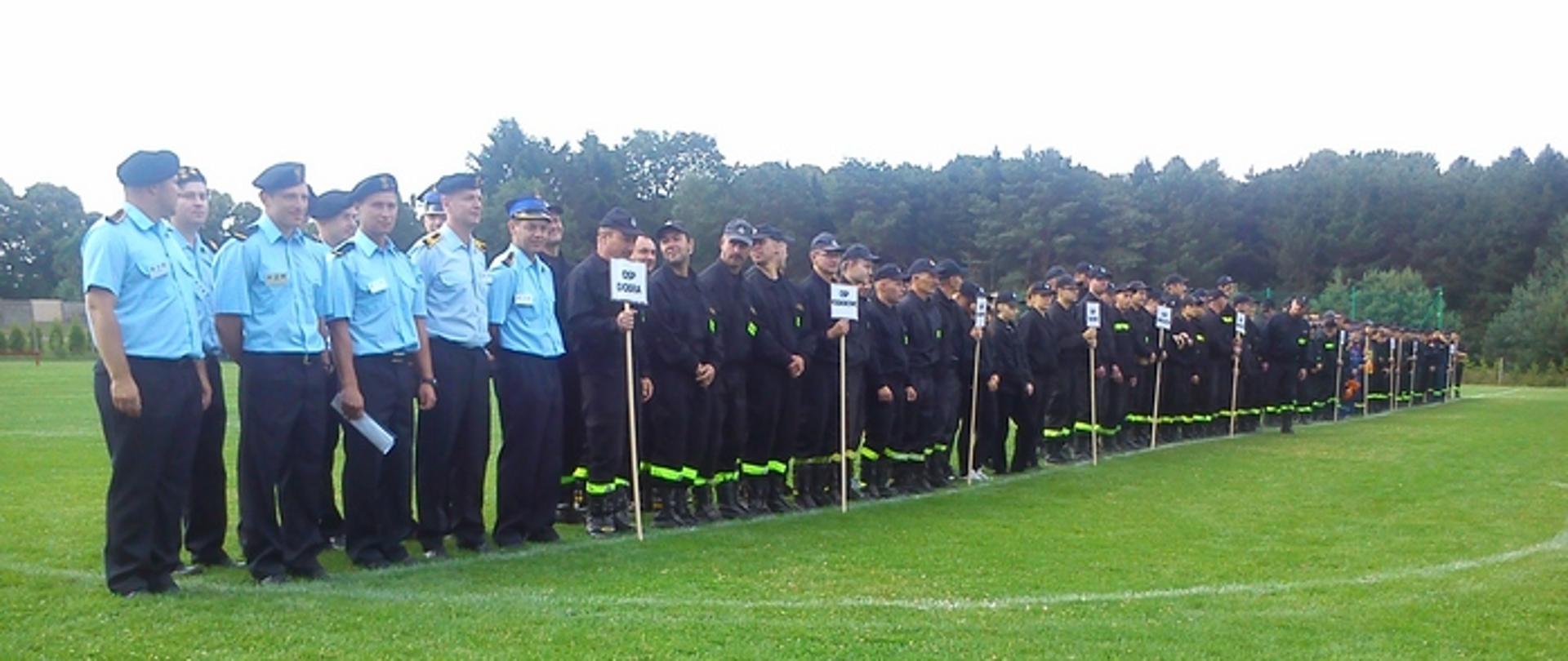 Zdjęcie przedstawia drużyny oraz sędziów zawodów ustawionych w dwuszergu na boisku