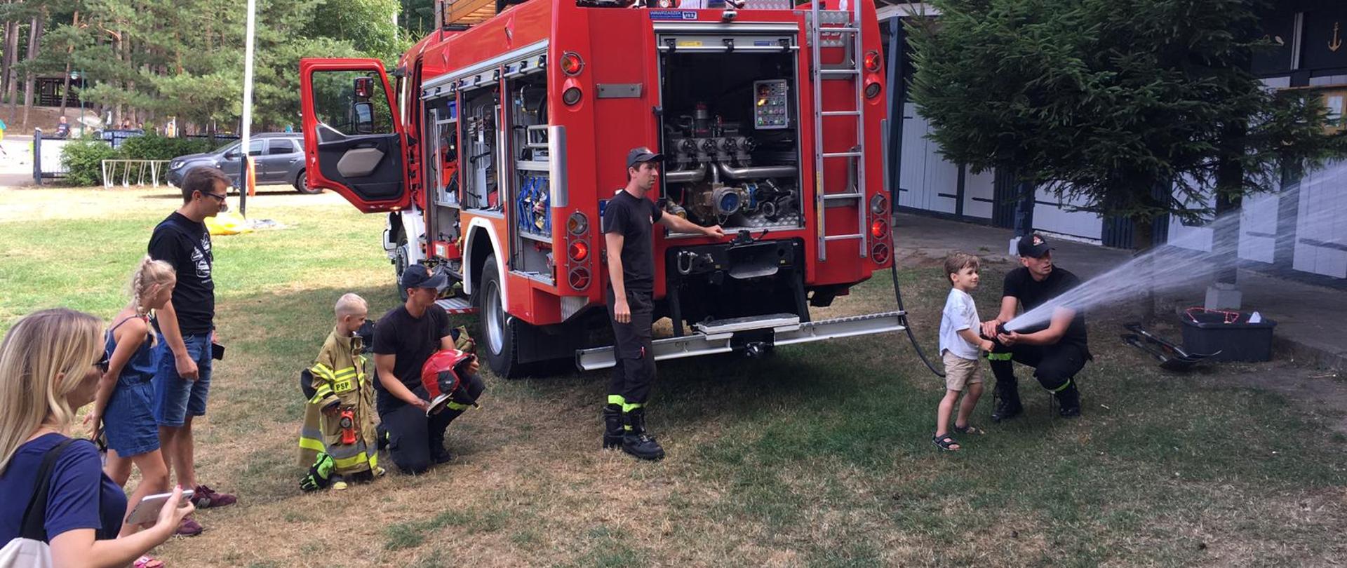 Strażacy pokazuje dzieciom jak lać wodę z prądownicy 