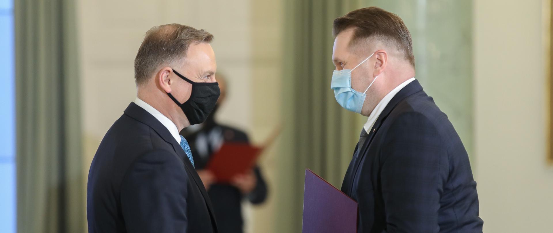 Minister i prezydent, w maseczkach, ściskają sobie ręce.