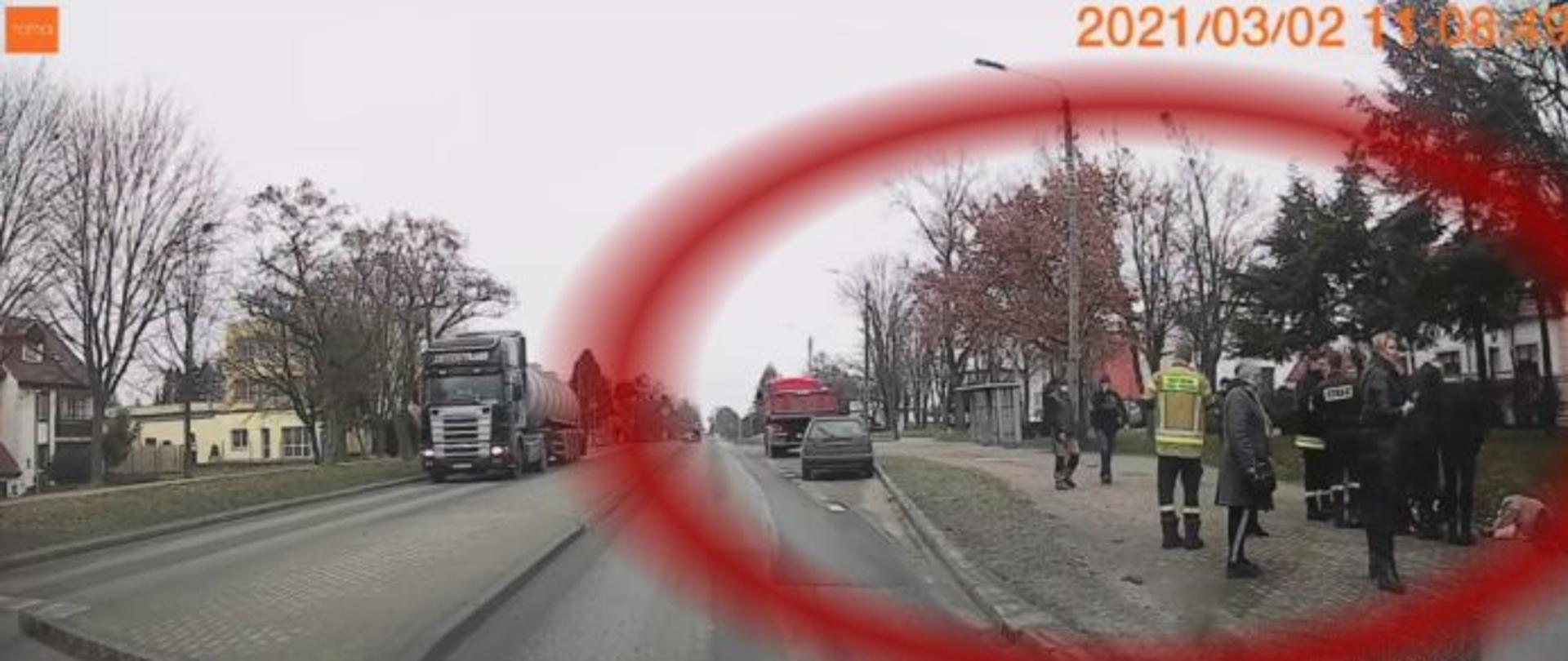 zdjęcie robione z wnętrza przejeżdżającego auta, po prawej stronie widać funkcjonariuszy PSP oraz kilkoro gapiów.