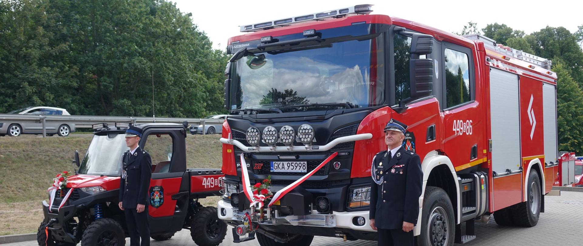 Druhowie ochotniczej straży pożarnej stoją obok pojazdów ratowniczych.