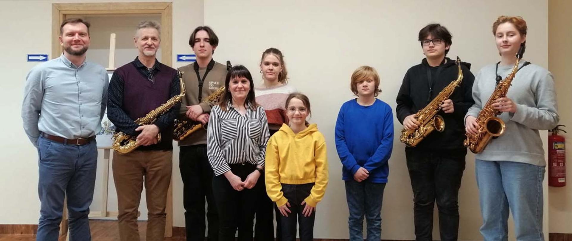 Uczestnicy warsztatów z saksofonami w auli, po lewej prowadzący warsztaty, nauczyciel klasy saksofonu i dyrektor szkoły.