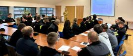 Zdjęcie wykonane wewnątrz pomieszczenia. Przedstawia grupę strażaków OSP podczas wykładu. 